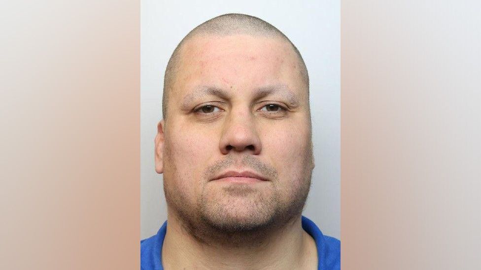 Police image of Cameron MacKay who is wearing a blue top and has a shaven head