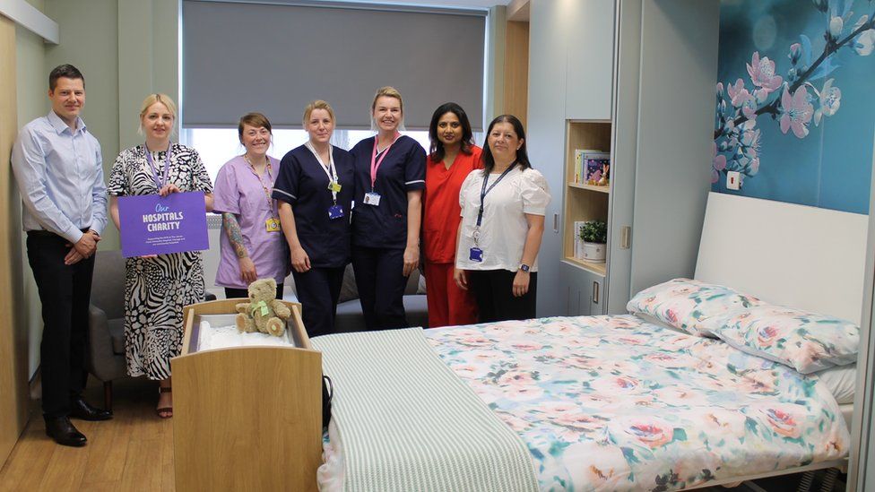 A group of people pose beside a bed and cot