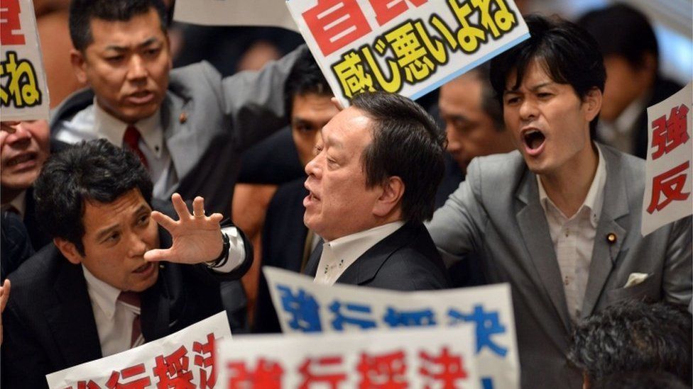 Yasukazu Hamada (C), chairman of a parliamentary panel on Japanese Prime Minister Shinzo Abe's controversial security bills, is surrounded by opposition lawmakers holding placards which say "Opposed to forced passage of the bills", during a parliamentary committee discussion on the bills at the National Diet in Tokyo on 15 July 2015