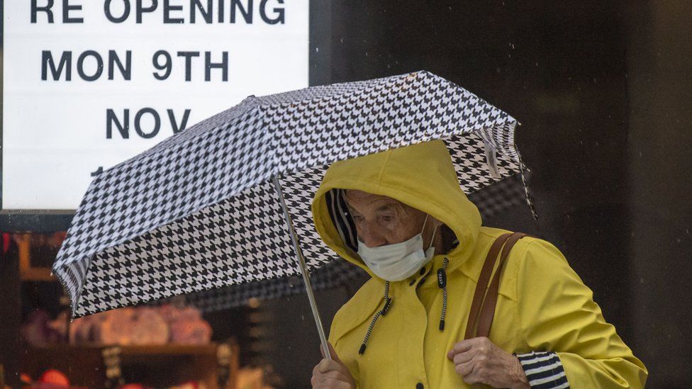 A woman wearing a face mask walks past a shop with a sign in the window saying 'opening Mon 9th Nov' on November 1, 2020 in Cardiff, Wales