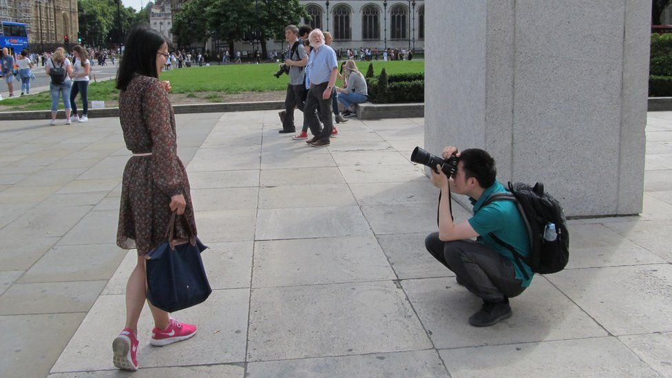 A man kneeling down to take a woman's photograph