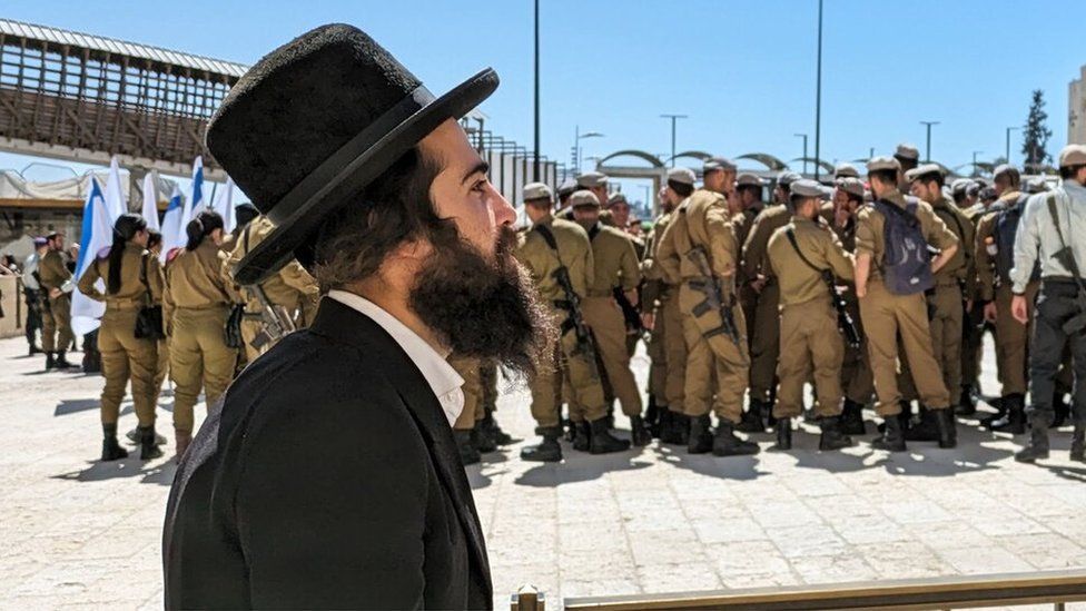 An ultra-Orthodox man walks past Israel soldiers (March 2024)