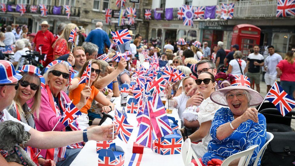 People smile and wave union flags at a street party in Swanage