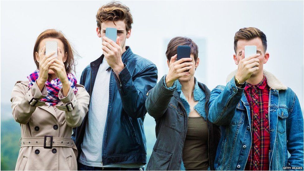 Four people holding their smartphones in front of their faces