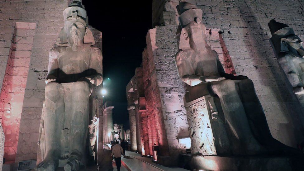 People walk between two large sculptures at night in Luxor, Egypt - Wednesday 24 November 2021
