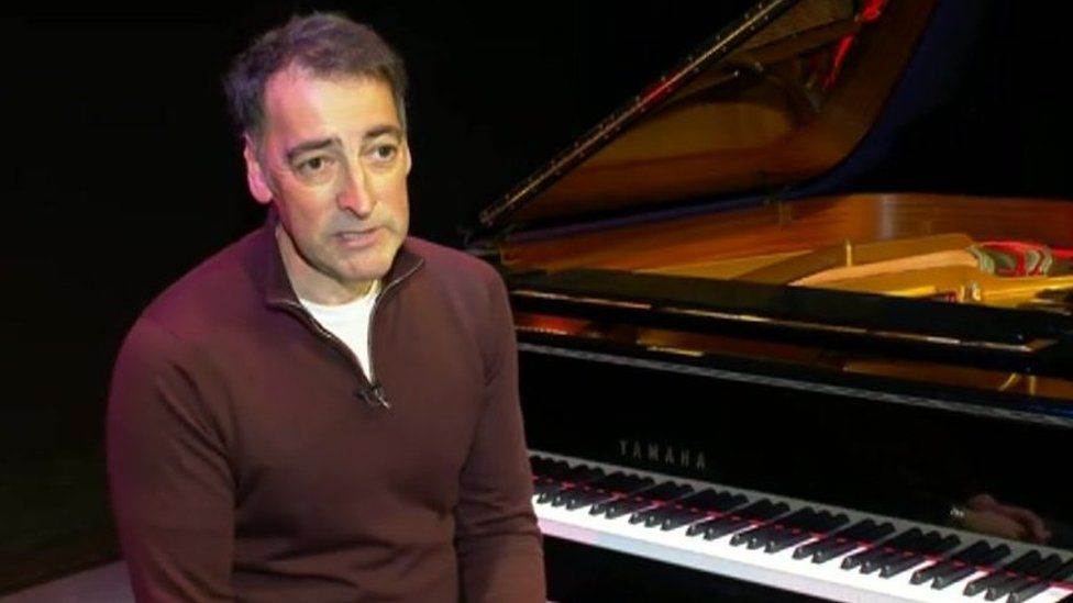 Alistair McGowan sitting in front of a piano