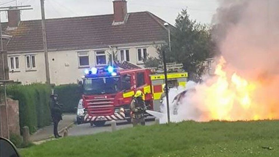 Car on fire with fire engine and armed police in attendance