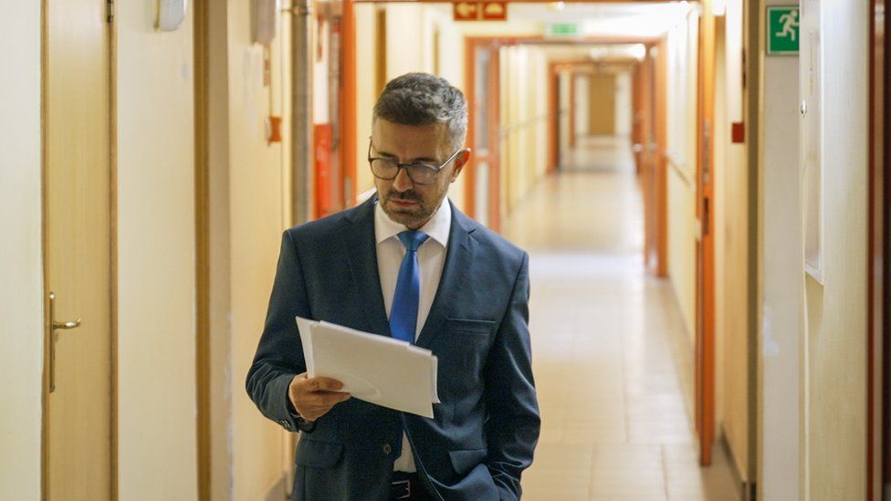 News presenter Zbigniew Luczynski stands in a corridor reading notes