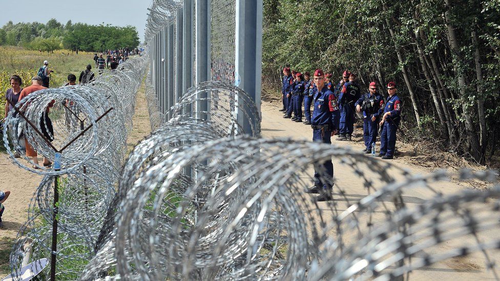 Migrants and refugees walk near razor-wire along a 3-meter-high fence secured by Hungarian police (R) at the official border crossing between Serbia and Hungary, near the northern Serbian town of Horgos on September 15, 2015.
