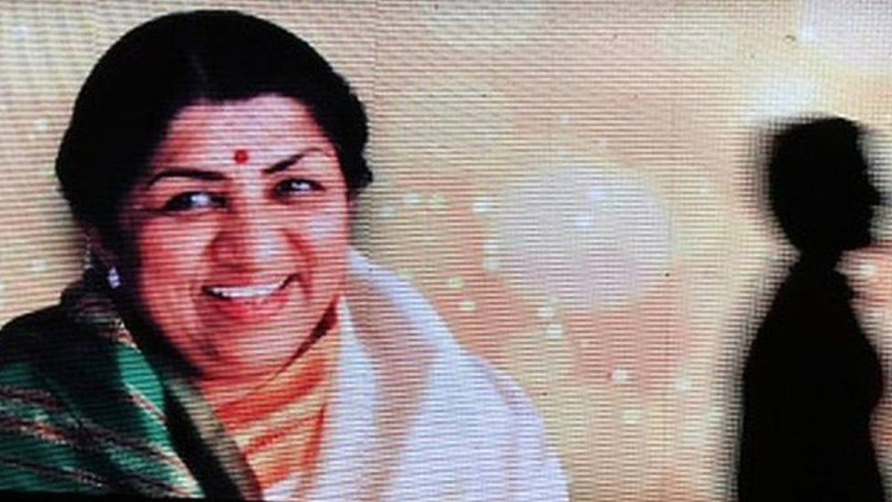 People walk past a LED display of legendary singer Lata Mangeshkar who passed away in Mumbai. The legendary singer was hospitalised and taken to an Intensive Care Unit (ICU) as her health deteriorated. she passed away on 6th February 2022 at the age of 92