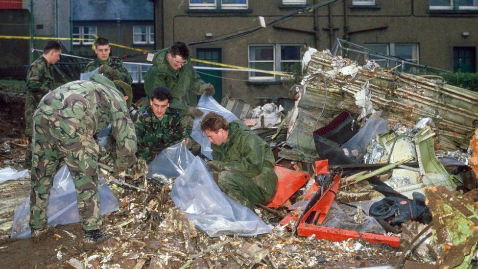 Men in military uniforms sift through debris on a housing street