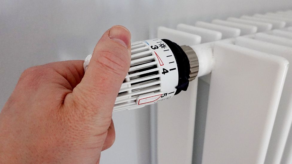 Hand on the heating thermostat of a radiator
