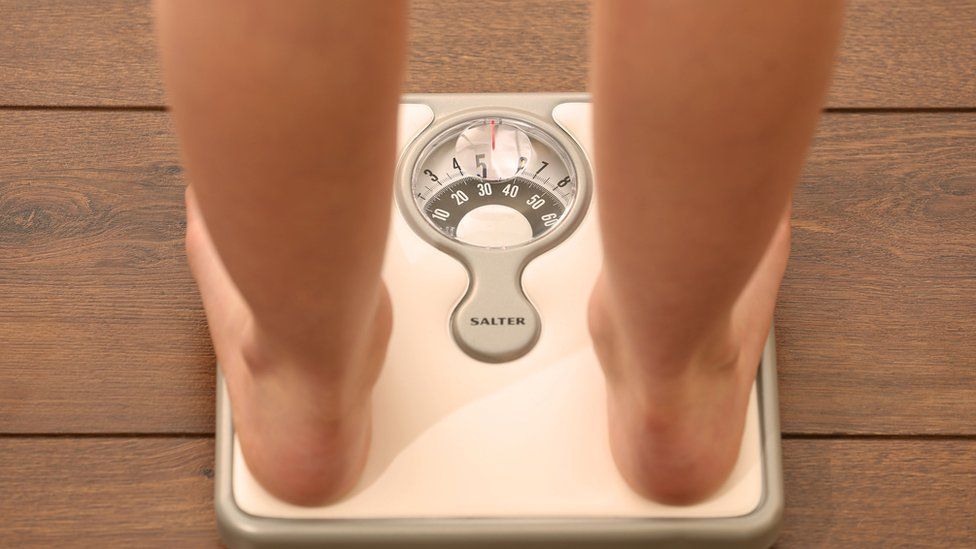 Young girl weighing herself on bathroom scales, checking her weight