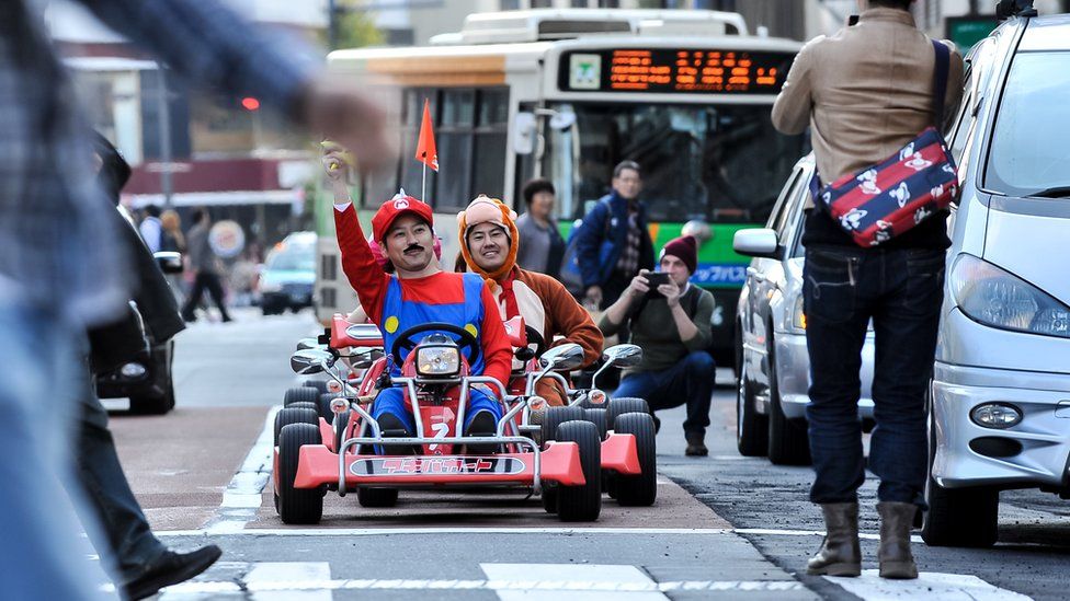 Люди фотографируют участников, которые ездят по Токио в персонажах Mario Kart для мероприятия Real Mario Kart в Токио, 16 ноября 2014 г., Токио, Япония
