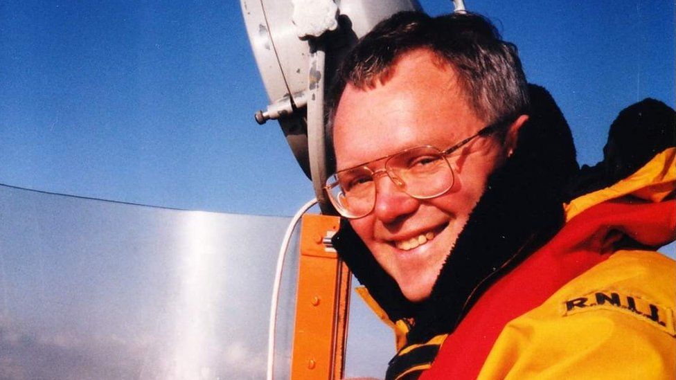 Geoff Cowan, in yellow lifeboat jacket, smiles at the camera