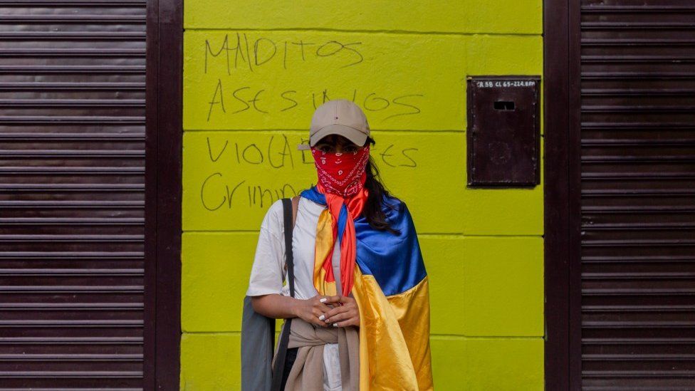 Протестующий стоит перед граффити с надписью «Проклятые убийцы, пороги, преступники» в Медельине 19 мая 2021 года
