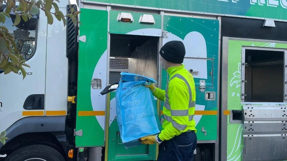 Back of man in high-vis putting a bag of recycling into a lorry
