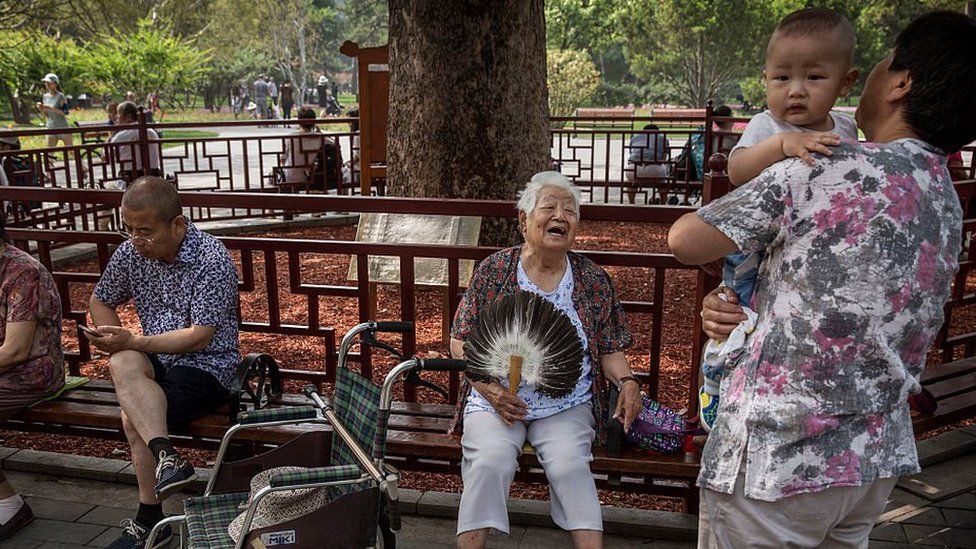 An elderly Chinese woman laughs with a man carrying a baby in Ritan Park on June 10, 2016 in Beijing, China.