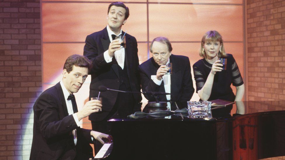 Comic actors (L-R) Hugh Laurie, Stephen Fry, John Bird and Jane Booker standing around a piano, in a sketch from the BBC series A Bit of Fry and Laurie, 1994.