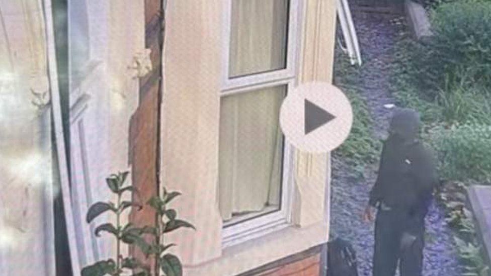 CCTV footage obtained by the BBC showing a man thought to be the suspect outside a hostel. A man is seen dressed in black looking in the window of a building.