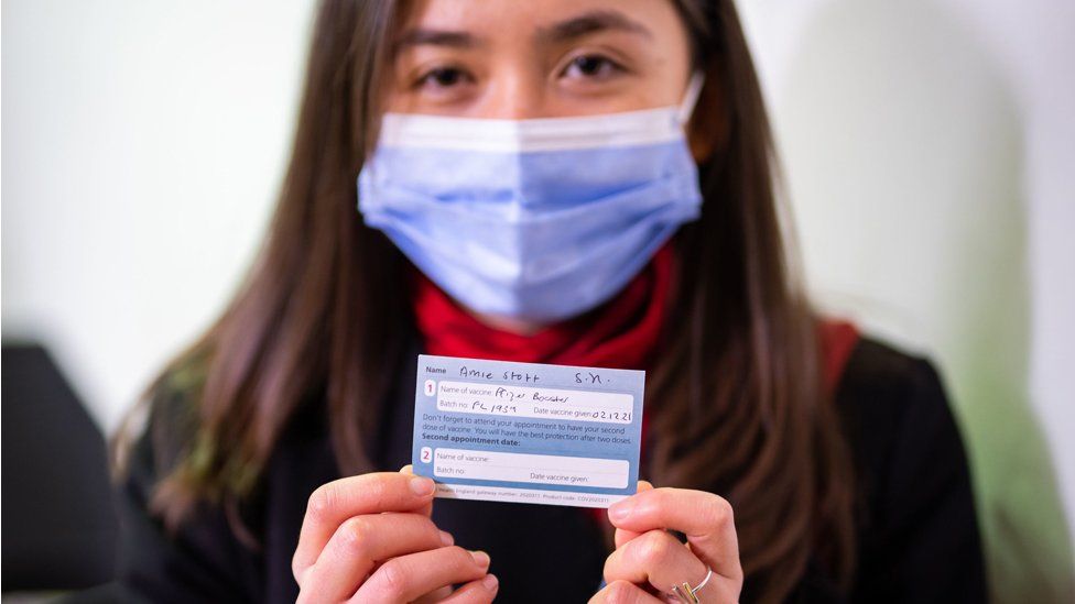 A woman holds up her vaccine record card during a trip to get a booster jab