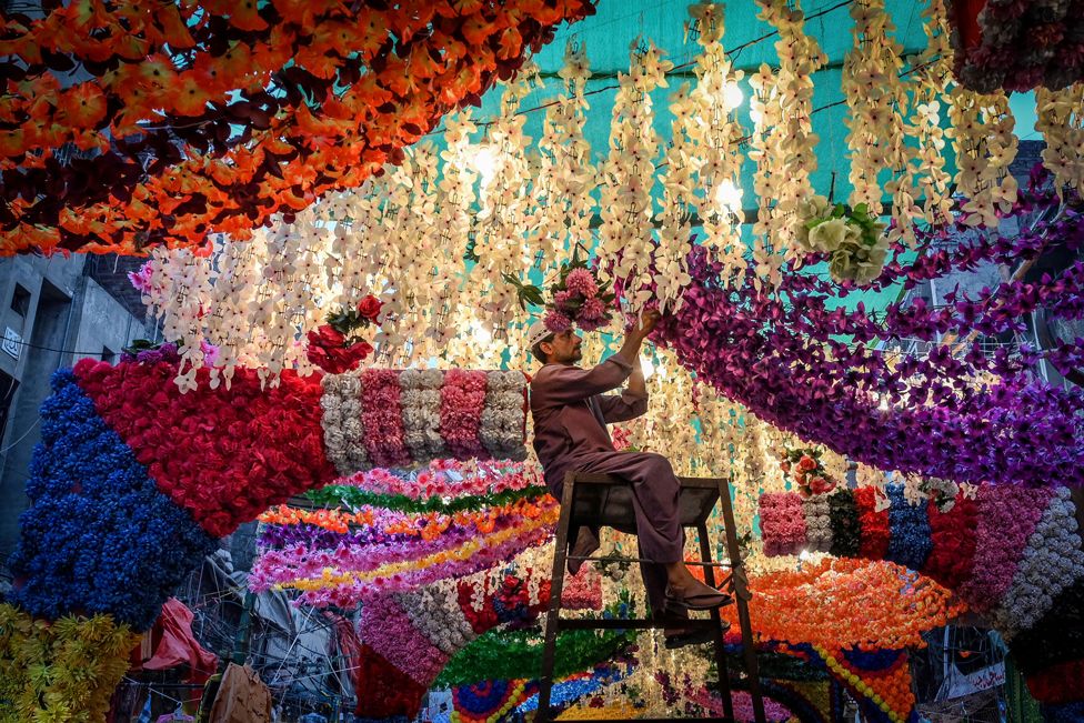 A man installs floral decoration at a market place in Lahore, Pakistan, on 17 October 2021, ahead of the celebrations for Eid-e-Milad-un-Nabi which is the birthday of Prophet Mohammad