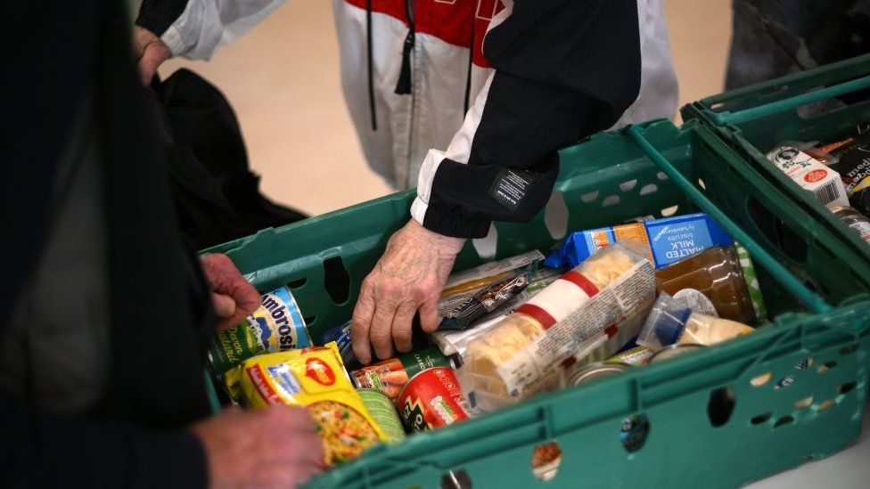 Photo from October 2022 showing an anonymous man reaching into a basket of donations at Hackney Foodbank.