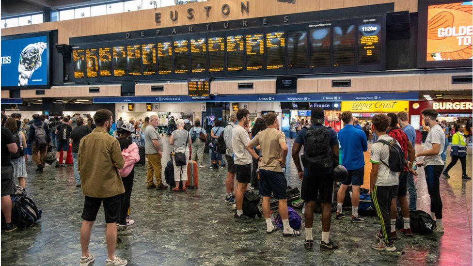 Rail passengers wait for announcements at Euston train station in July