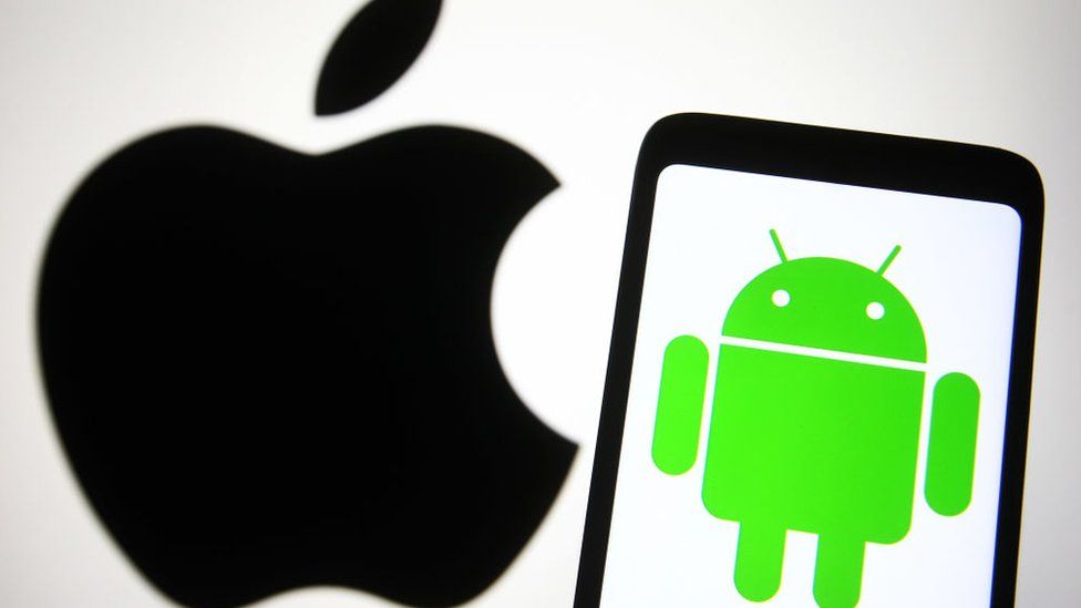 Логотип Apple отображается на заднем плане, а логотип Android находится на телефоне ближе к камере