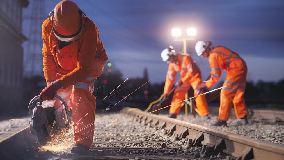 Railway maintenance workers using grinder on track at night