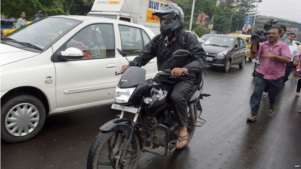 Индиец Сиддхарт Дас (слева) пытается избегать средств массовой информации, путешествуя на своем мотоцикле по оживленной дороге в Калькутте 1 сентября 2015 года.