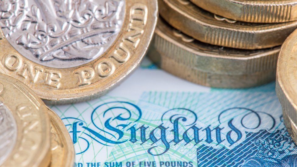 Слово «Англия», изображенное на английской банкноте в 5 фунтов стерлингов, окруженной стопками недавно отчеканенных фунтов стерлингов
