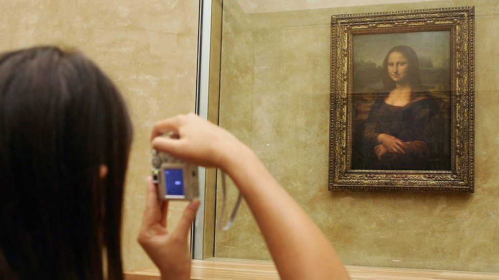 Woman taking a photo of Mona Lisa in the Louvre