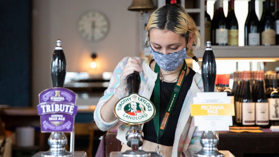 A woman working in a pub, wearing a mask