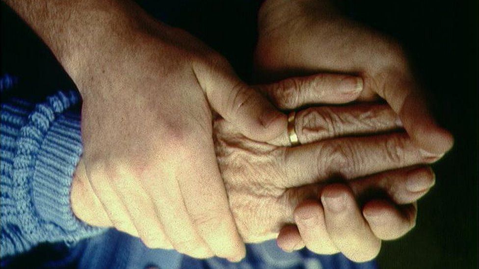 Elderly patient and carer holding hands