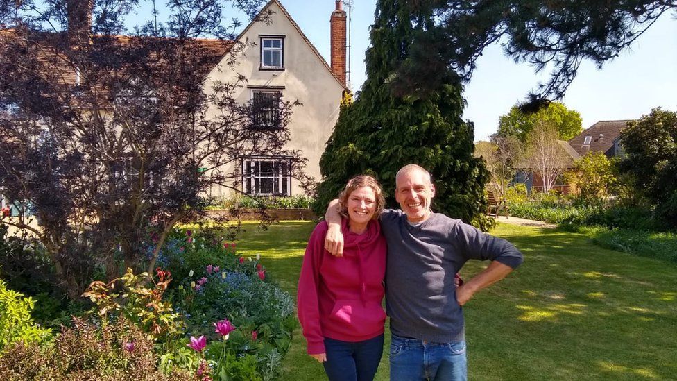 Peter Dutch with his arm around a woman. They are standing in a garden which has flowers, trees and grass.