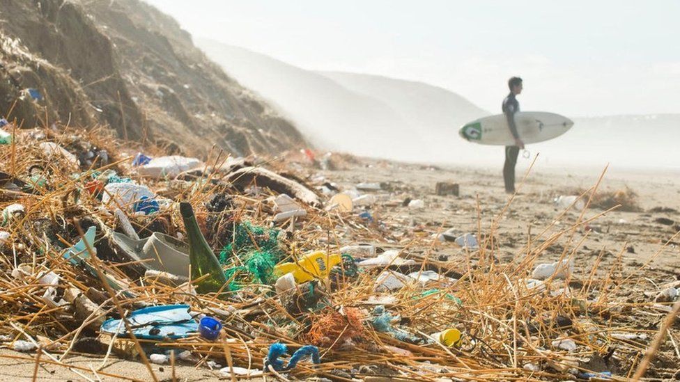 A surfer stands near a mound of plastic litter on a beach in Cornwall
