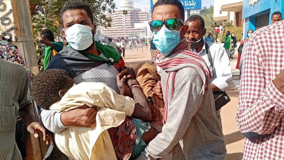Суданские протестующие бросаются на помощь раненому демонстранту после того, как силы безопасности применили слезоточивый газ во время митинга, посвященного трем годам начала массовых демонстраций, которые привели к изгнанию сильного человека Омара аль-Башира в столице Хартуме 19 декабря 2021 года. .