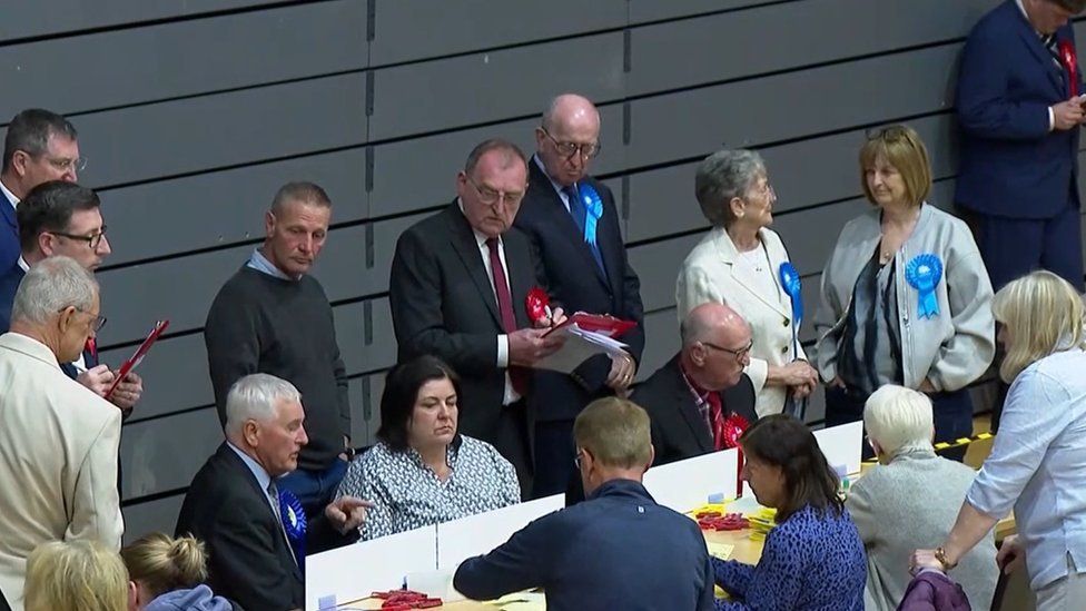 Candidates looking sombre as people count votes sitting at a table