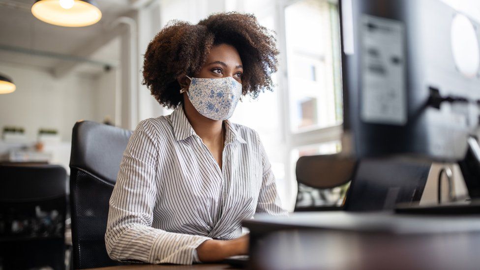 A woman wearing a facemask at a laptop