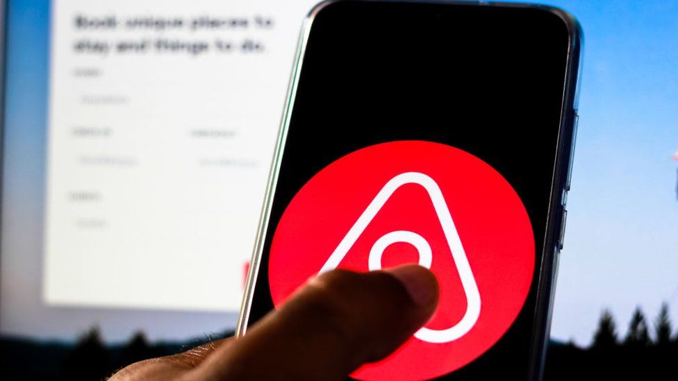 The AirBnB logo on a mobile phone held up in front of a computer screen showing the company's website