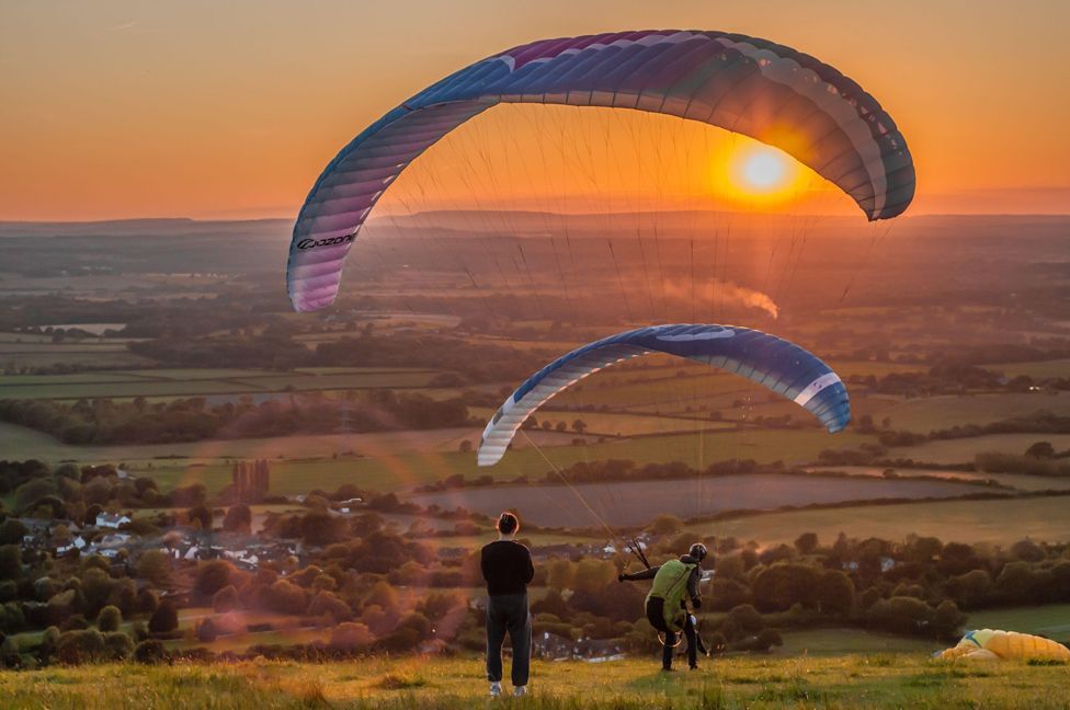 People paragliding at sunset at Devil's Dyke on the South Downs, Sussex, England, UK. 8th June 2024.