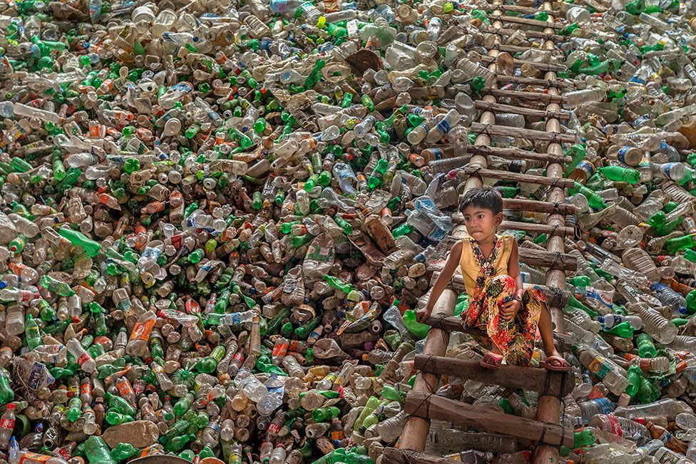 Un enfant est assis sur une échelle entourée de bouteilles en plastique dans une usine de recyclage de plastique à Chittagong, au Bangladesh