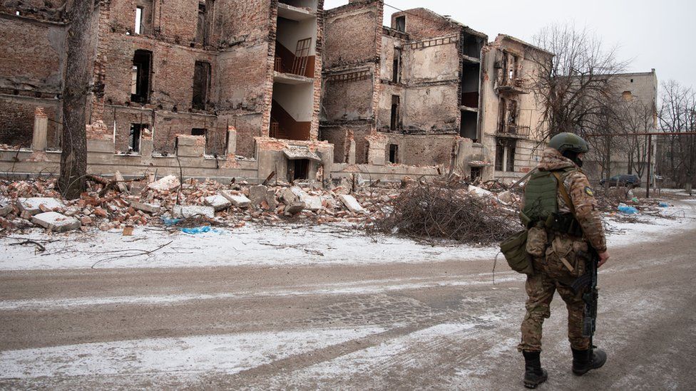 A soldier walks by a residential building in the town of Lyman
