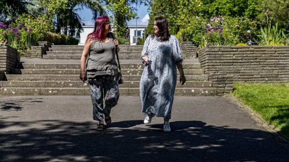 Two people win summery dresses walking in dappled light in the park