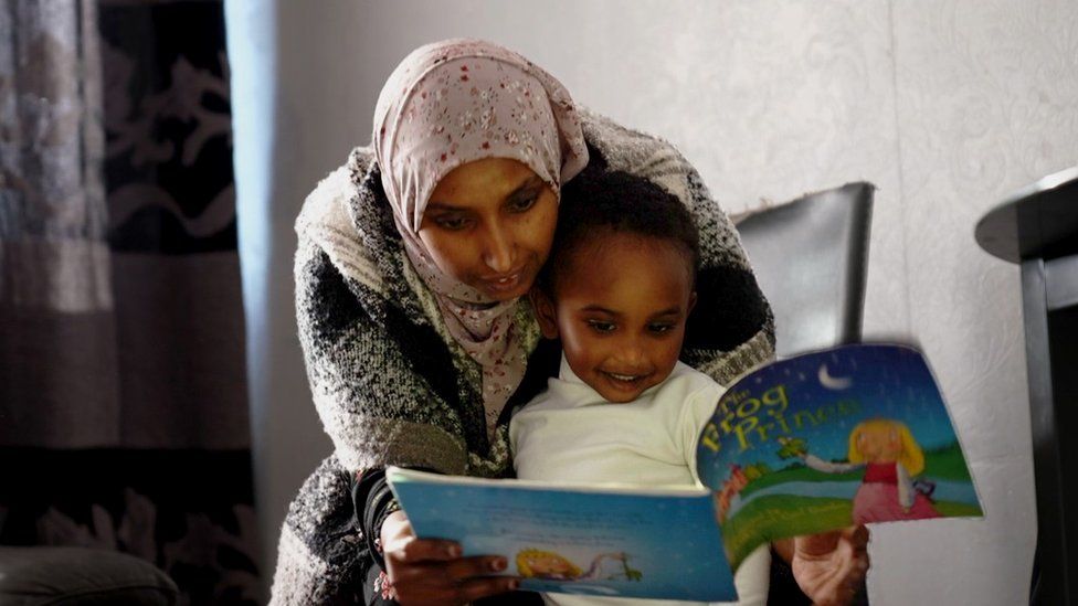 Photo shows Berlin Mirre and her youngest son reading a children's book