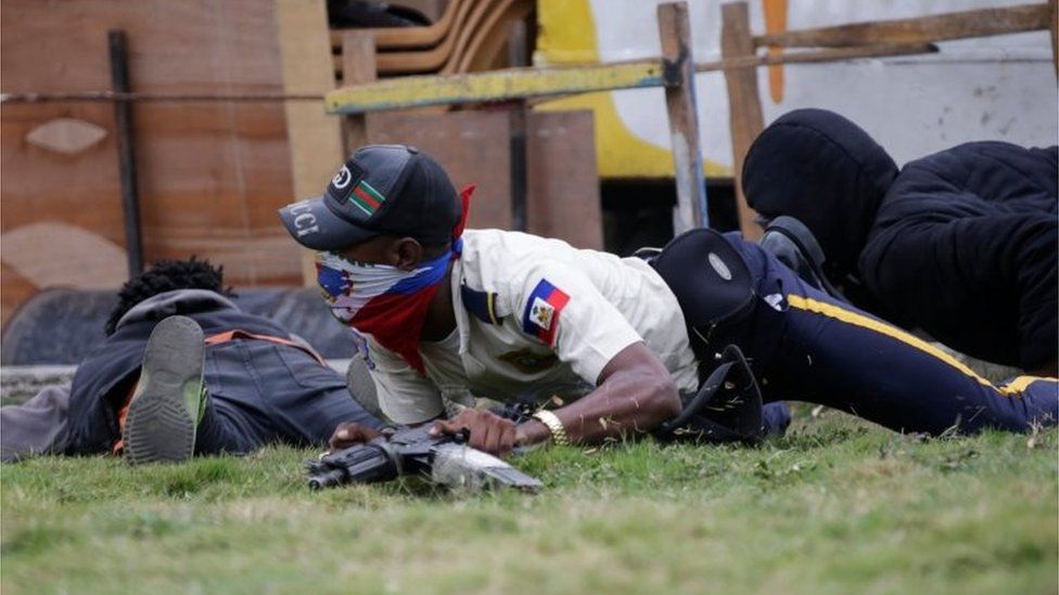 A masked man in a Haitian National Police uniform crawls on the ground during a shooting in Champ de Mars, Port-au-Prince, Haiti February 23, 2020