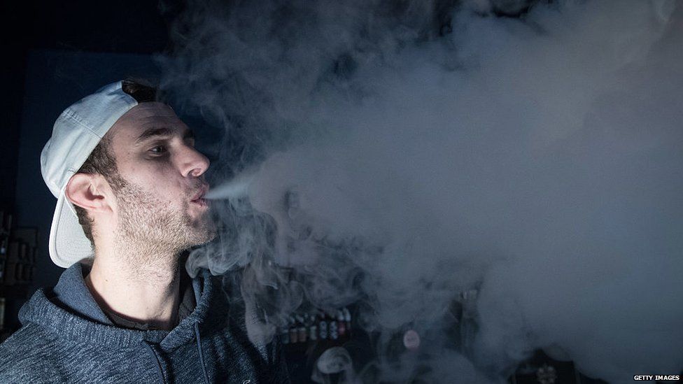 A man blowing smoke against a black background