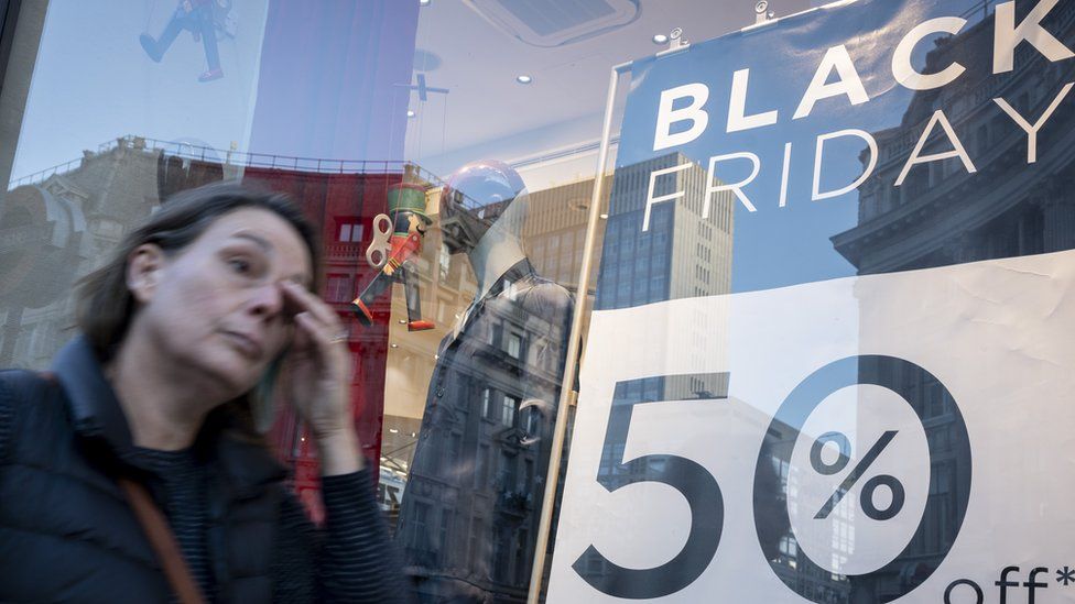 A woman looking stressed walking past a Black Friday discount sign in London