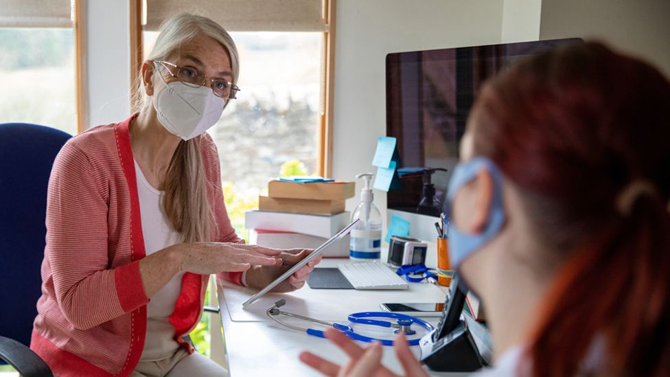 Stock image of a GP wearing a face mask talking to a patient